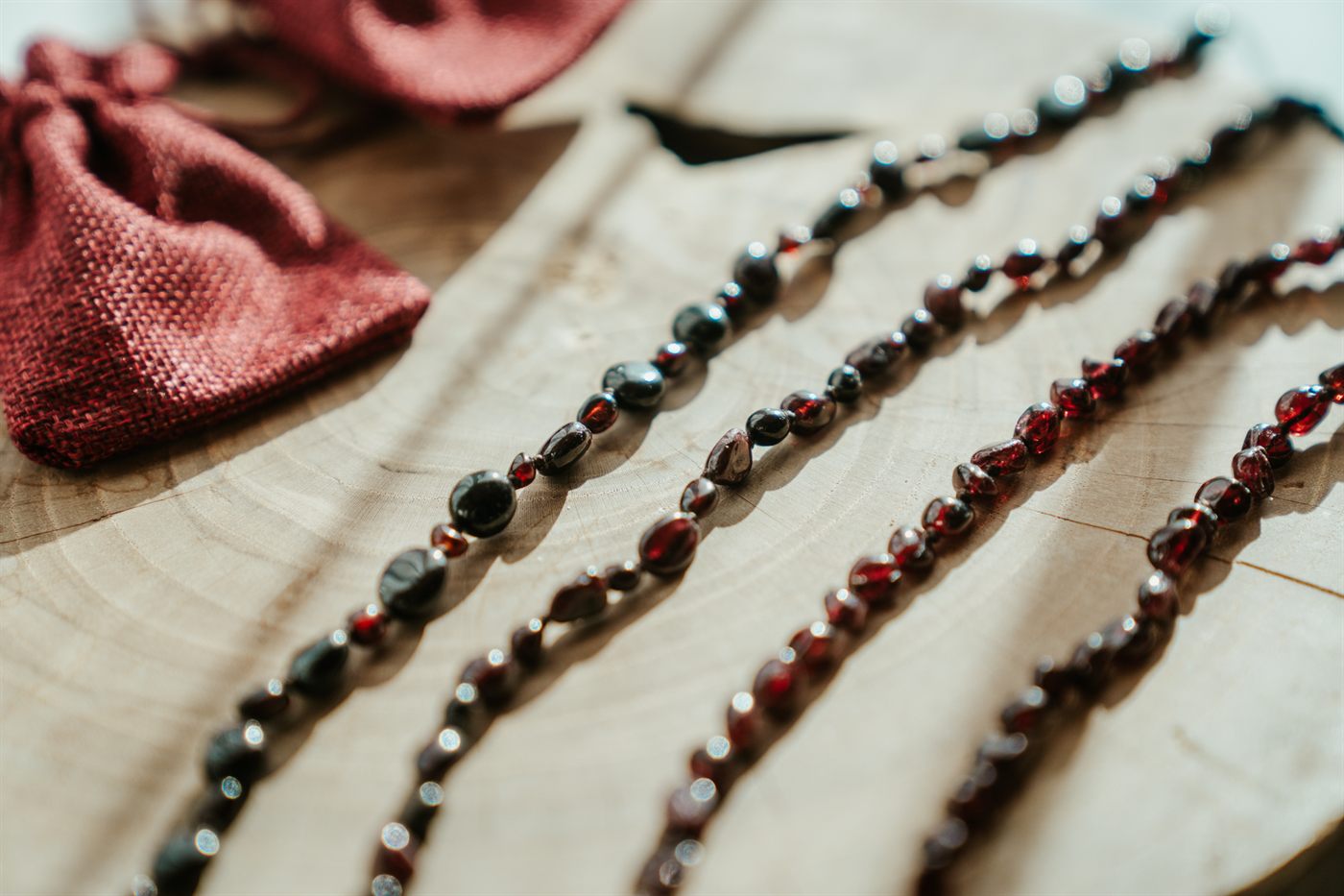 Four Moontime necklaces laid out on a wooden round beside their red pouches