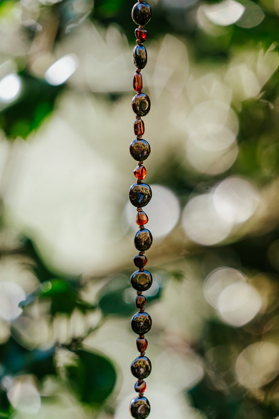 A Moontime necklace hanging among sunlit green leaves